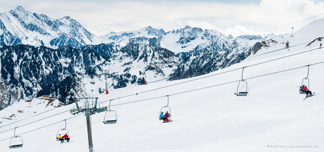 Wide view of skiers of 4-seat chairlift with mountain backdrop at Cauterets