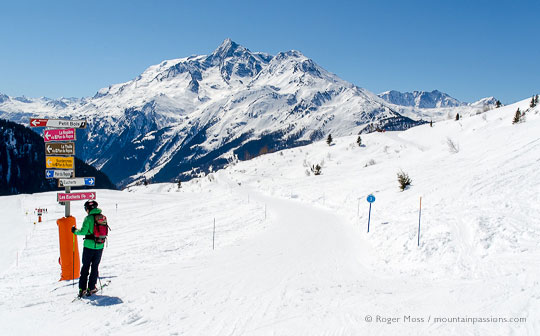 Skier beside piste signage with mountains