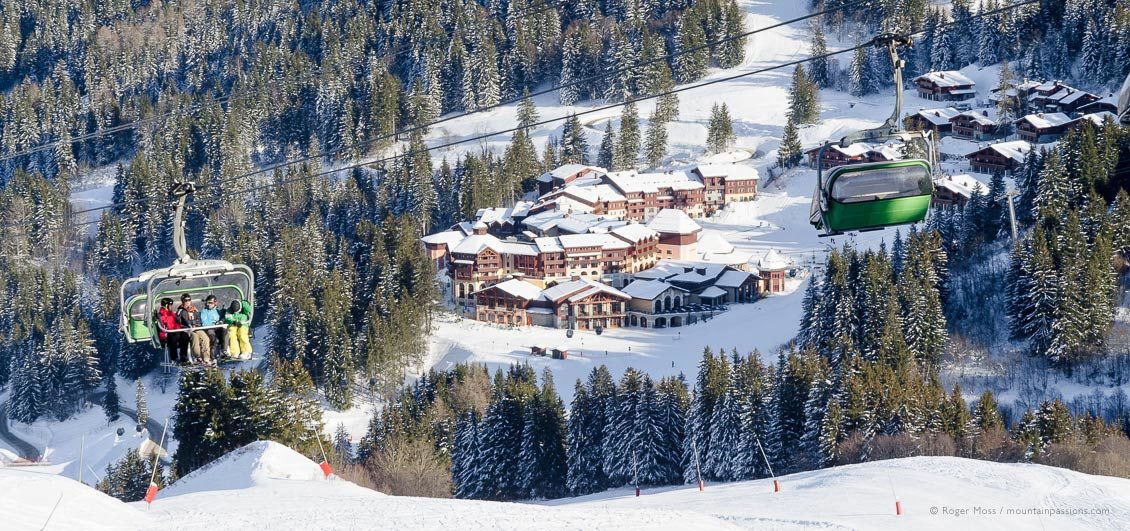 Skiers on chairlift with Club Med resort, Valmorel, French Alps