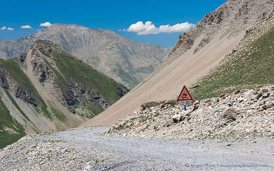 Wide view of mountain track with warning road sign and deep valley in background
