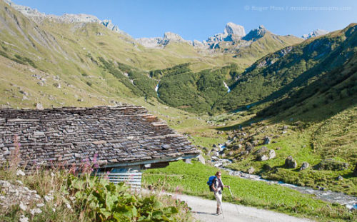 Walker passing mountain chalet near La Conchette, in summer in the Beaufortain, French Alps.
