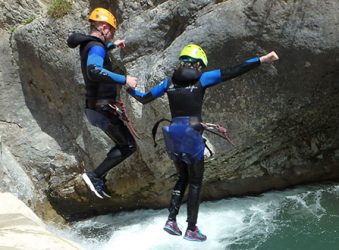 Canyoning couple holding hands, jump into pool.