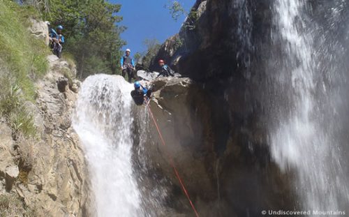Canyoning group watch person abseil over waterfall in southern French Alps