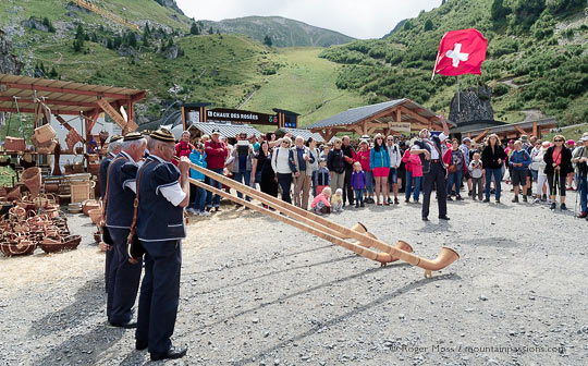 Alpine horn players with visitors surrounded by mountains at alpine festival above chatel, French alps