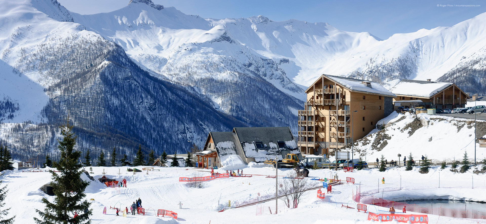 Wide view of children's ski school area, with apartments and mountains