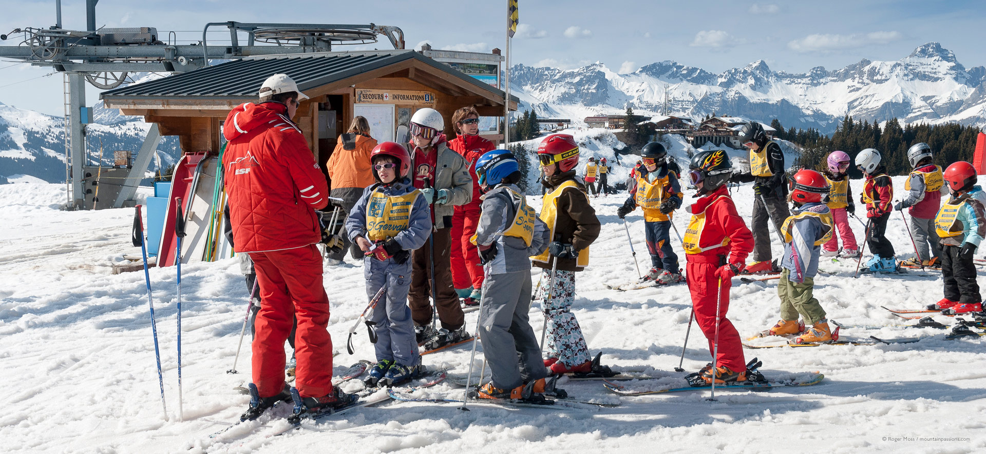 Young skiers gathering for ski lesson with ski instructor and mountains in background