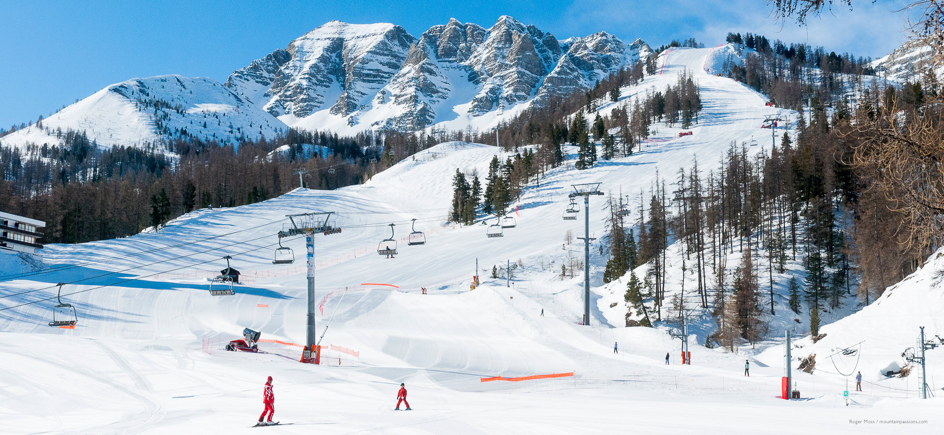 Early morning skiers on near-empty pistes, with trees and ski lifts