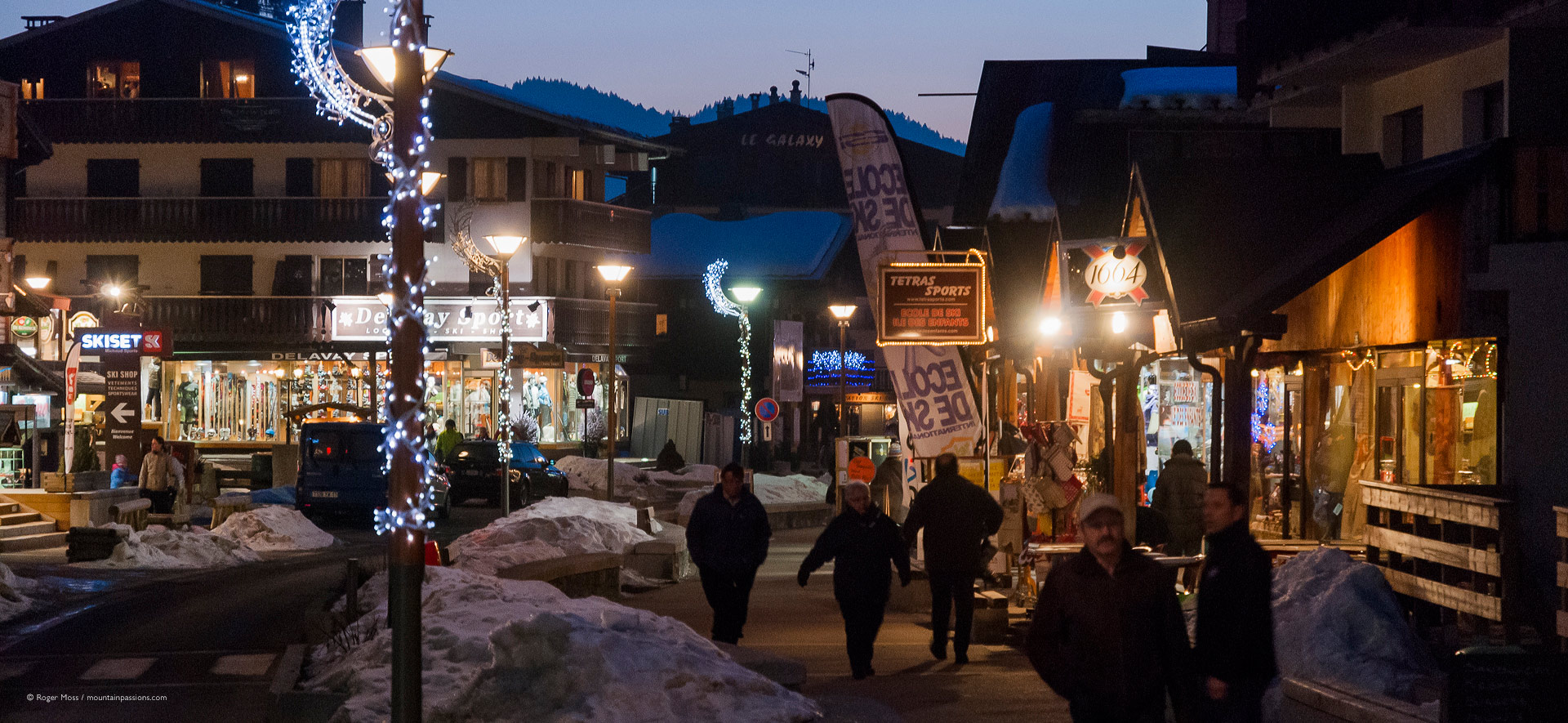 Visitors in village centre at dusk, with boutiques and ski shops.