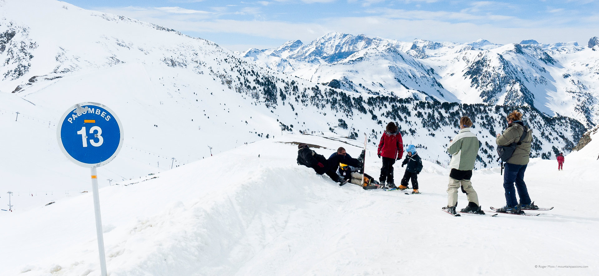 Family skiers adjusting snowboard bindings beside piste