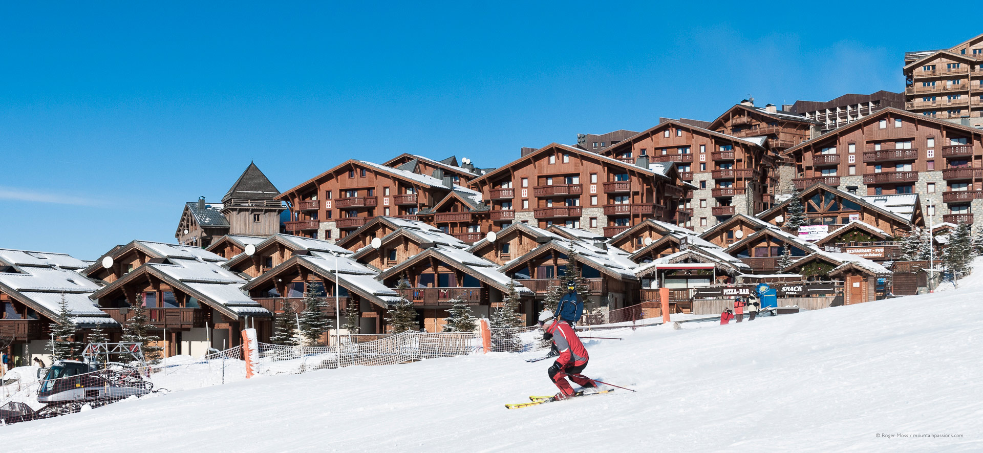 Skier passing recent chalet-style village development at Les Menuires.