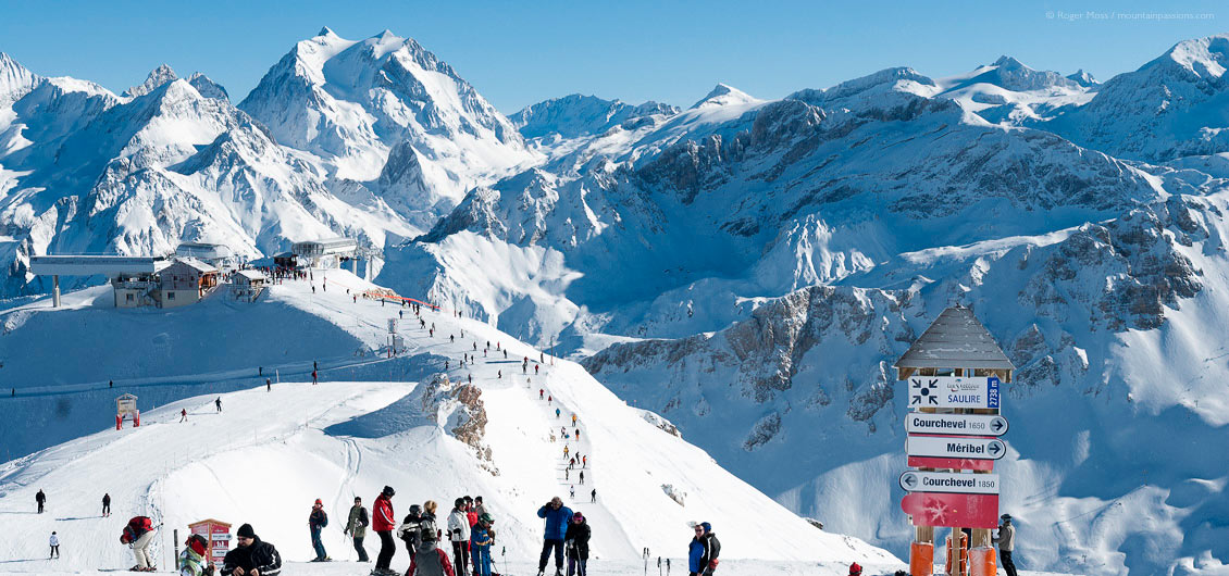Wide overview of skiers on ridge with ski lifts and mountain background, Meribel