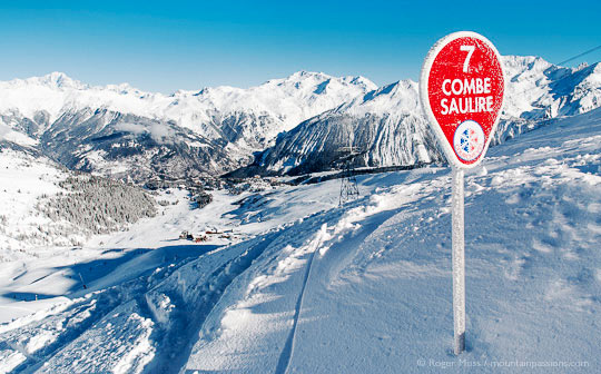 View past piste sign to snow-covered valley, ski village and mountains