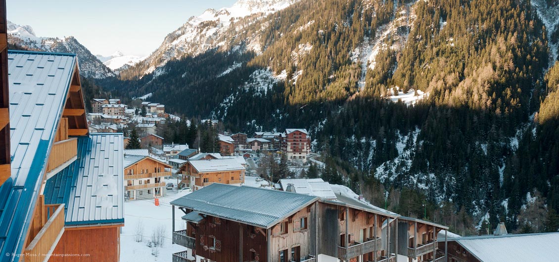 Overview of chalet-style ski village, valley and wooded mountainside