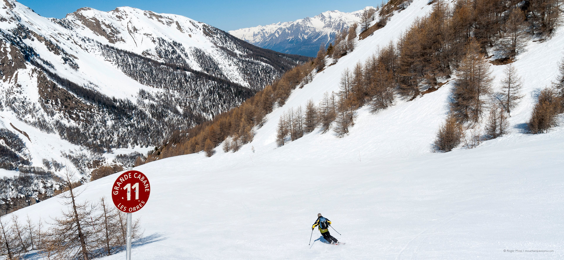 Lone skier descending red piste with beautiful mountain scenery.