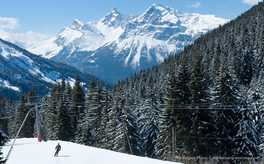 Skier at chairlift beside forest, with mountains in background