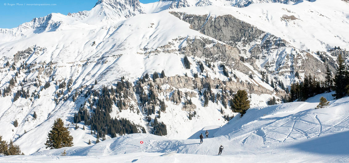 View of three skiers descending piste among rugged mountain scenery