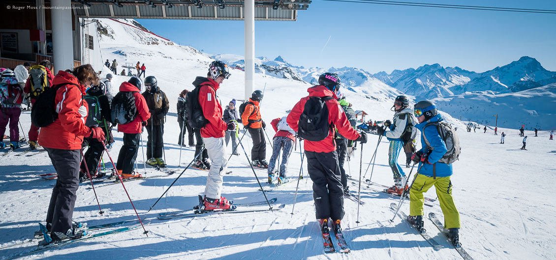 Large group of skiers leaving gondola lift top station with mountains in background