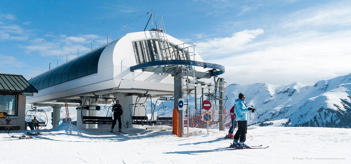 Skiers leaving high speed chairlift with snowy mountain background