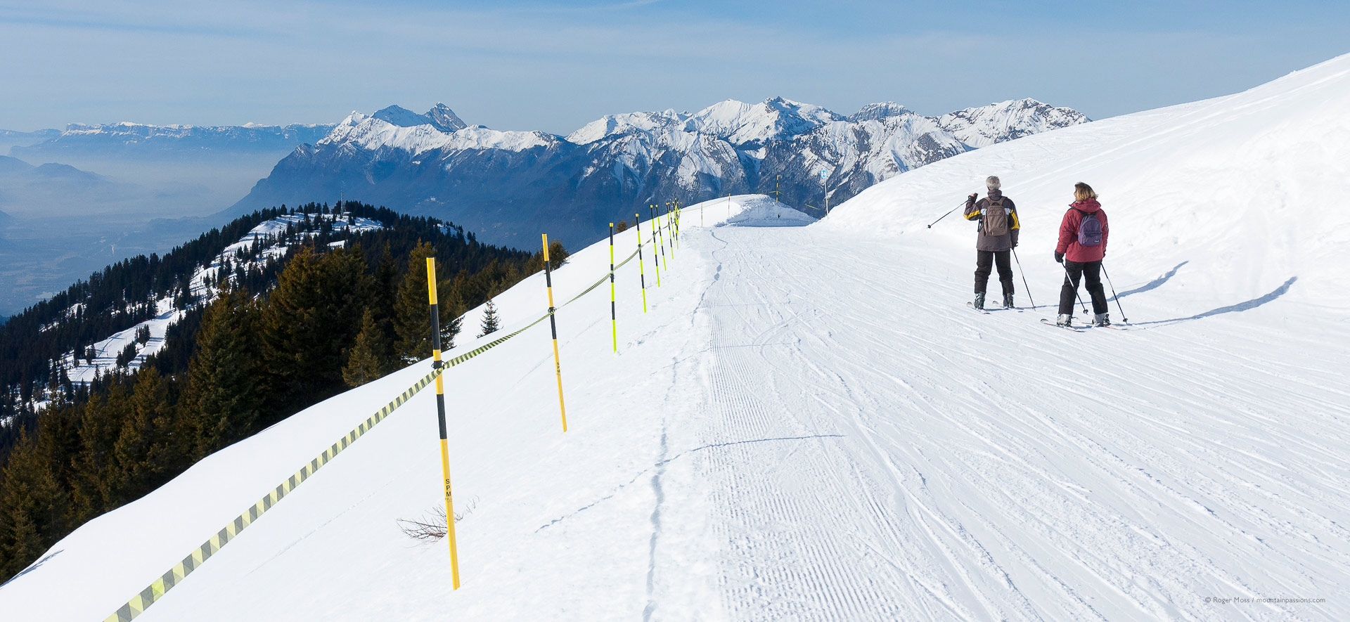 Close view of two skiers on piste, showing Espace Diamant ski area, above Crest Voland.