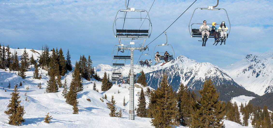 Wide view of skiers on chairlift above trees and ski terrain