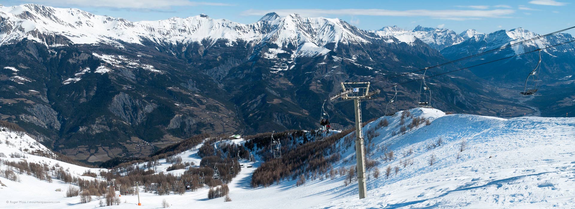 High, wide view of ski lift on mountainside with surrounding valleys at Pra Loup