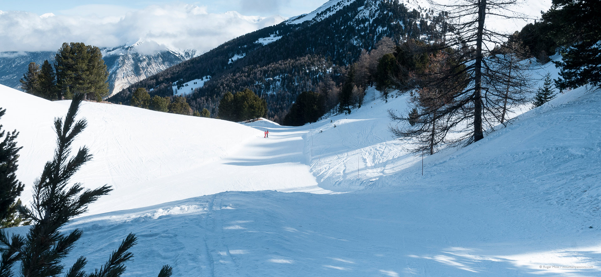 Wide view of piste with two skiers in distance.