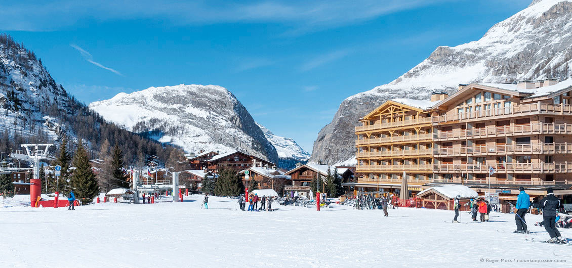 Wide view of skiers passing village apartment blocks, hotels and restaurants