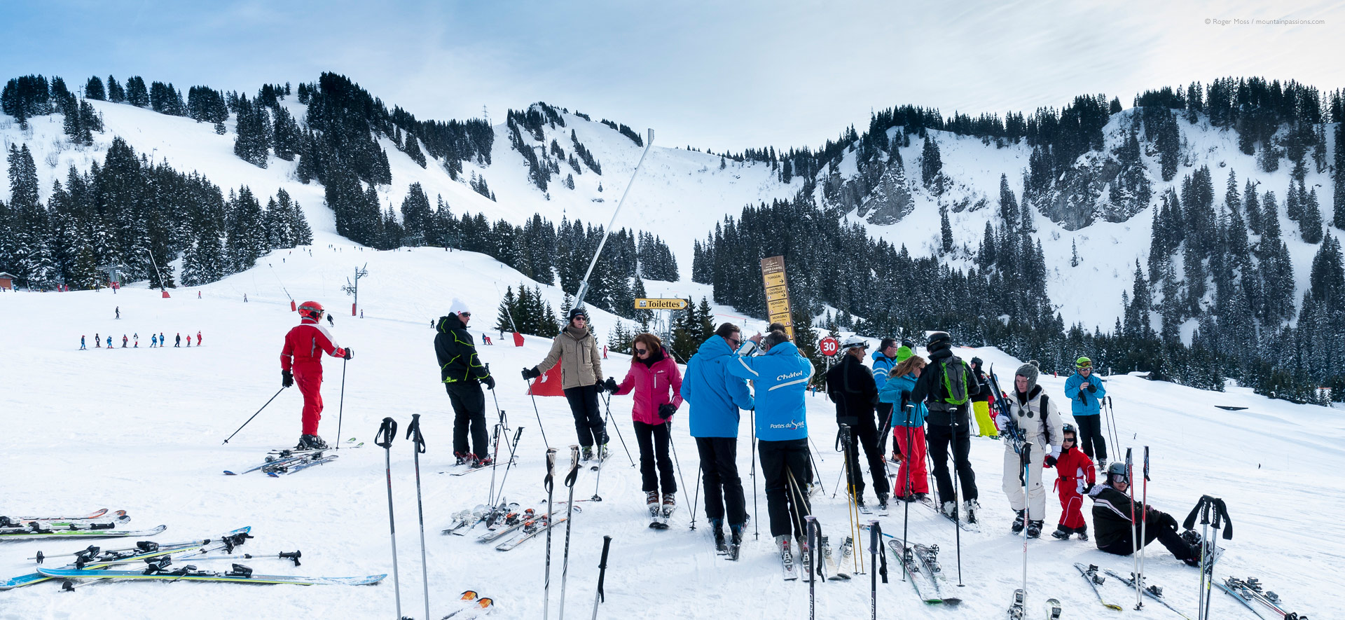 Group of skiers gathered beside pistes with mountains and forests in background at Chatel.