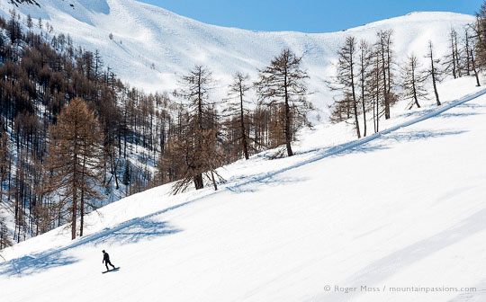 View from chairlift of snowboarder on piste with trees and mountains