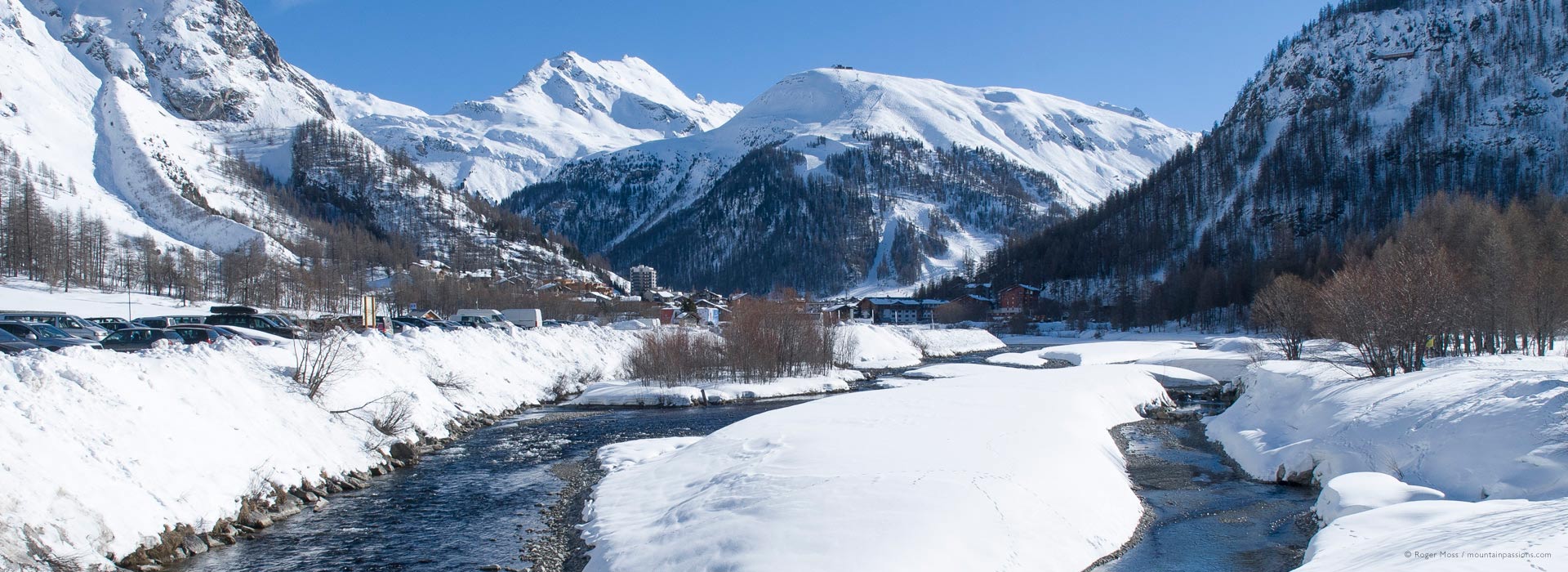 Wide view of river and snow-covered valley setting of Val d'Isere ski village.