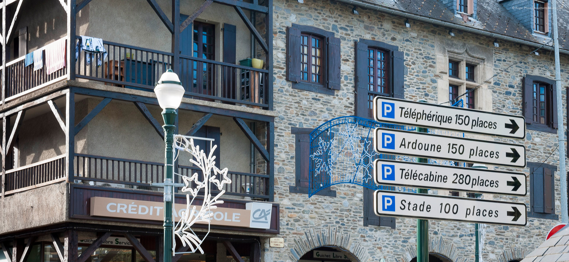 Low view of stone and timber facades, plus sign to ski lifts