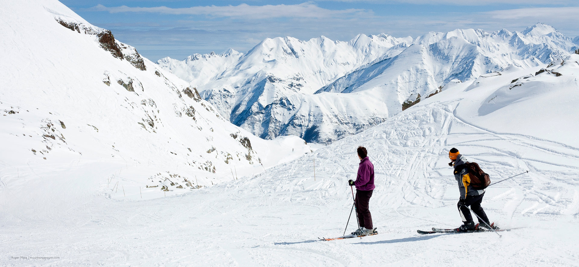 Two skiers on high altitude piste with big mountain views