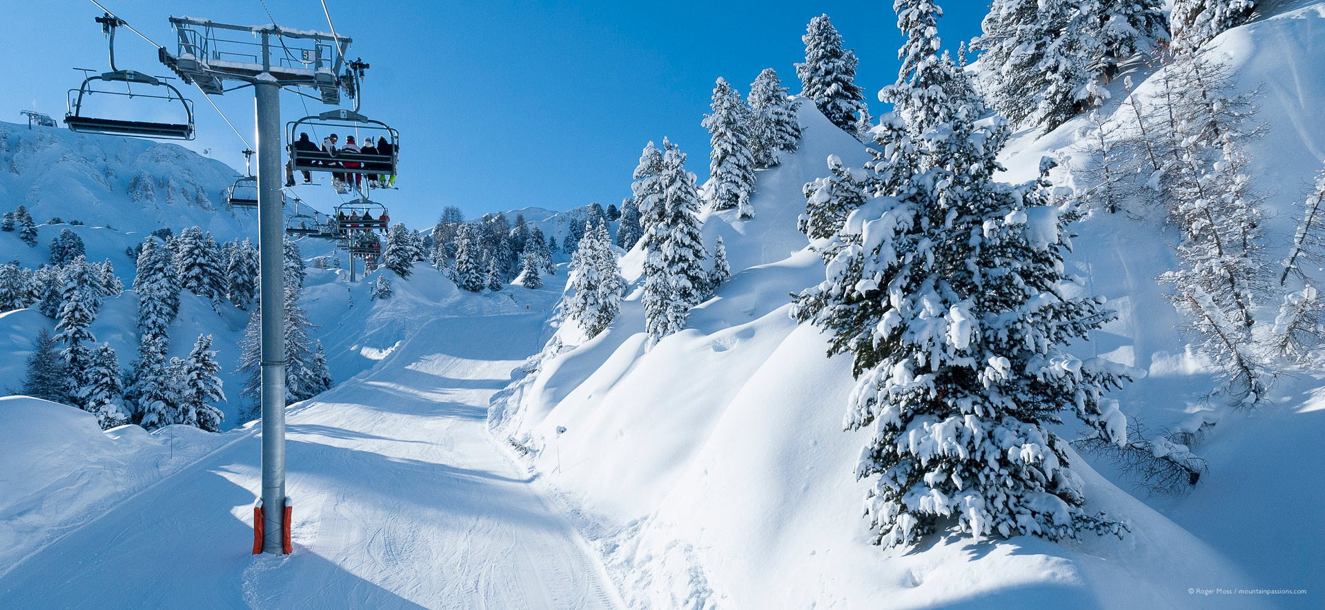 View from chair-lift of ski pistes and freshly snow-covered trees.