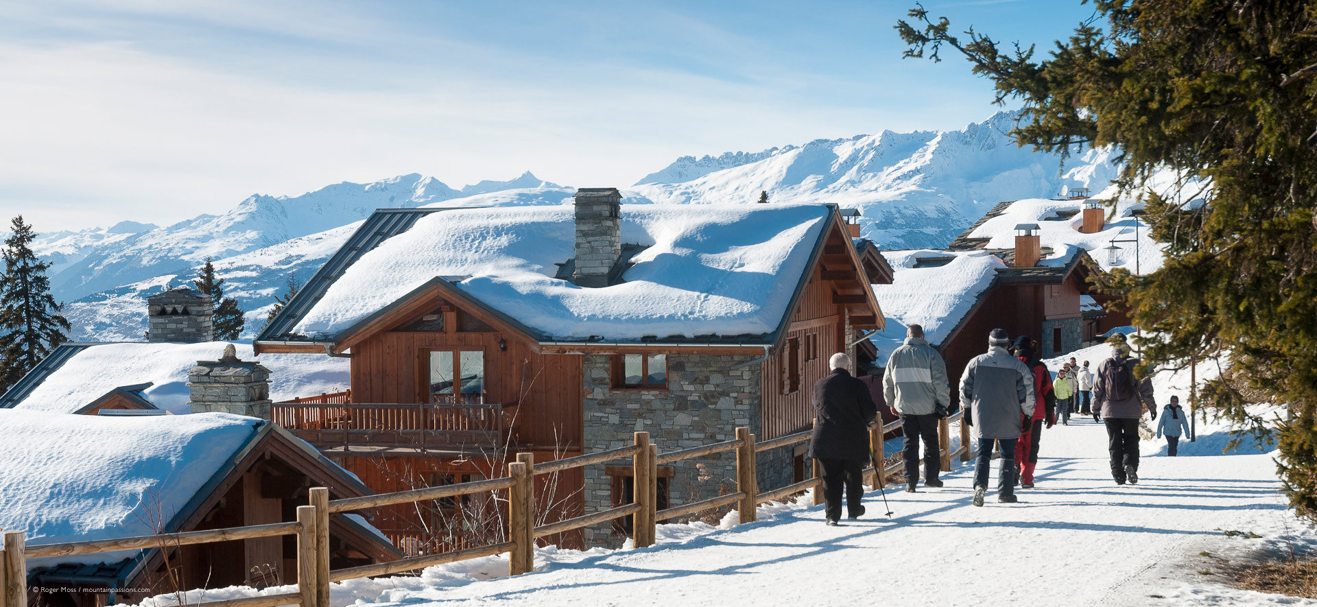 Late afternoon walkers on footpath with snow-covered chalets at La Rosiere.