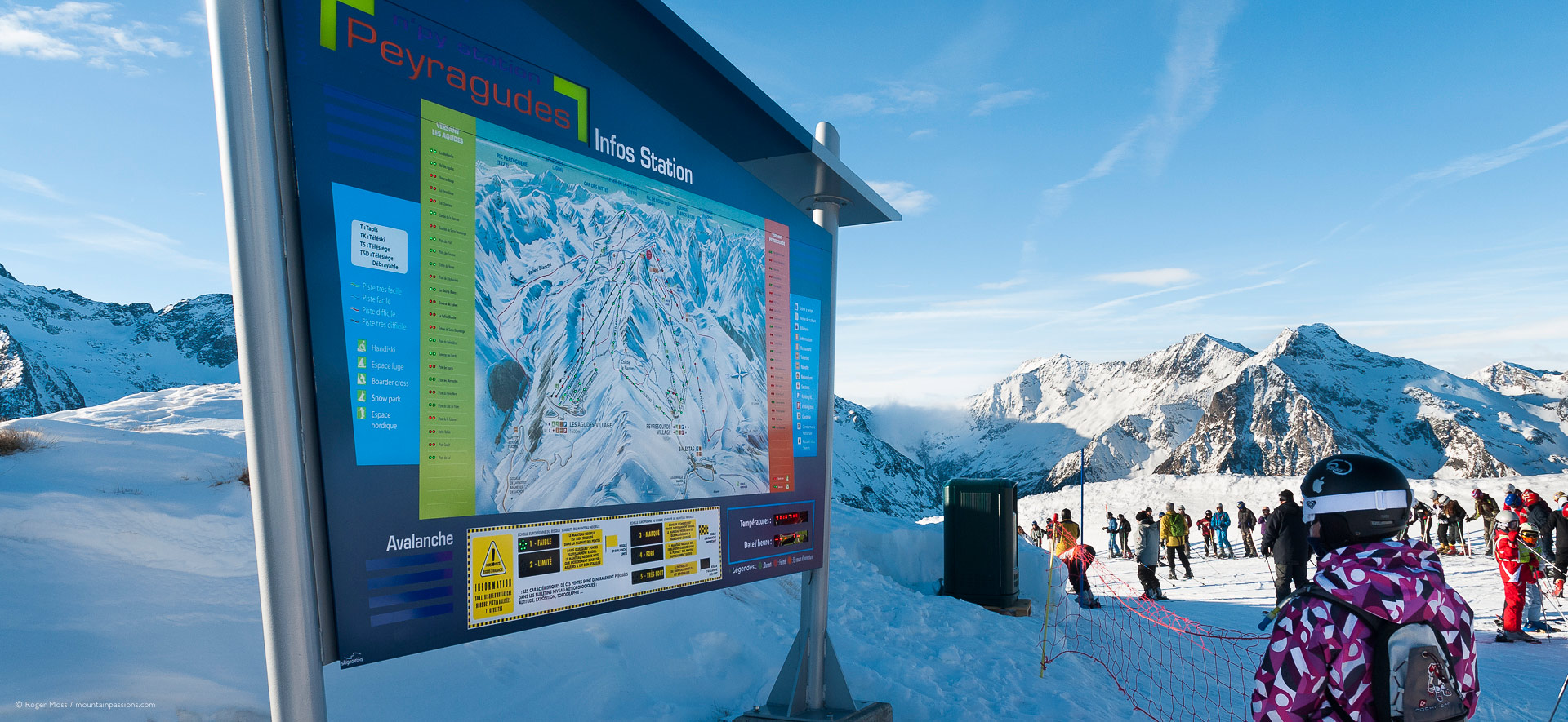 Young skier beside piste map sign.
