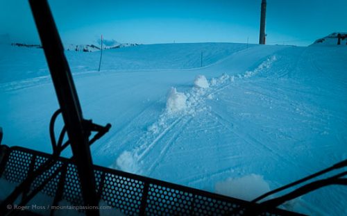 Driver's view from cab of groomer on ski piste at dusk