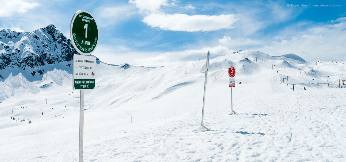 Wide view past ski school signs to mountains and pistes at Les Contamines