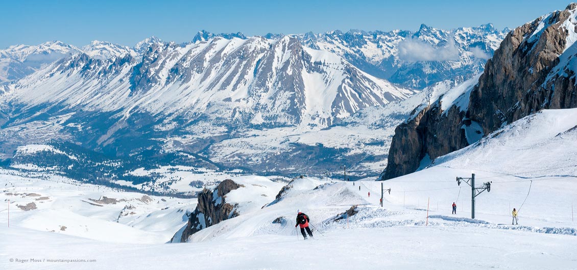 Wide view of skier on piste beside drag-lift with snow-covered valley and mountains in background