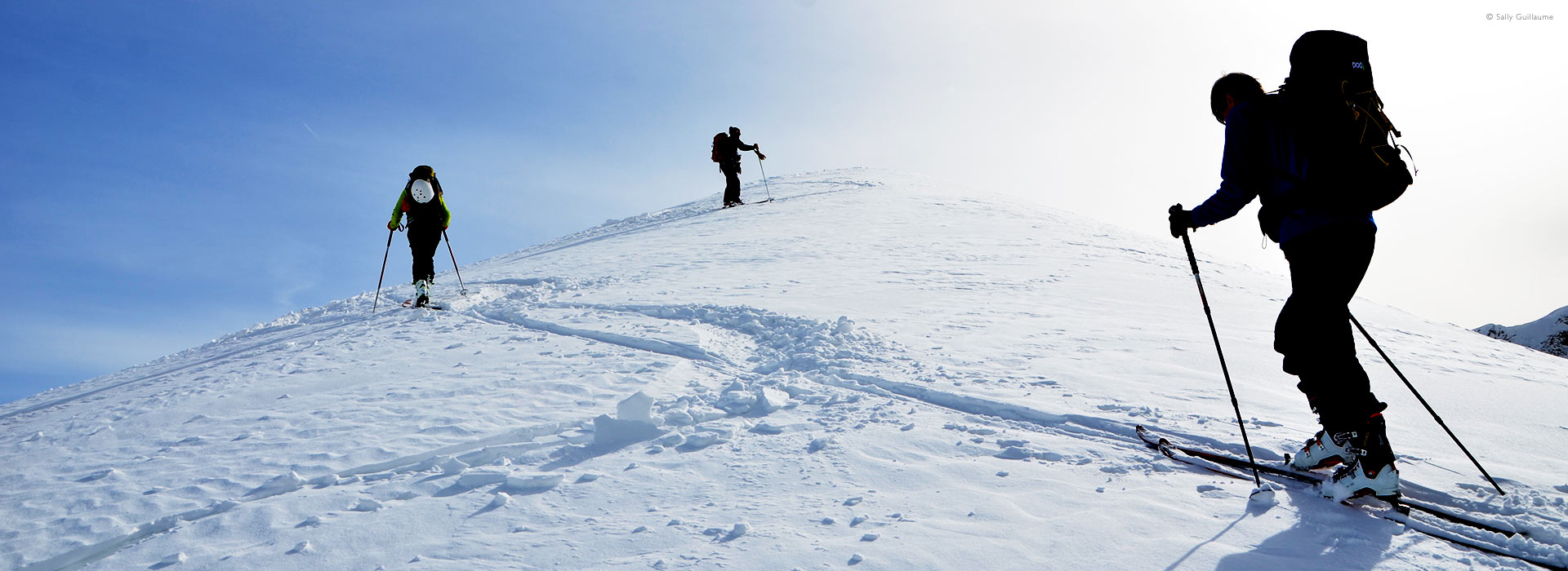 Low, wide view of ski-touring group nearing crest of mountain, French Alps