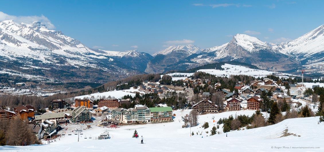 Wide overview of La Joue du Loup village, wide valley and snow-covered mountains