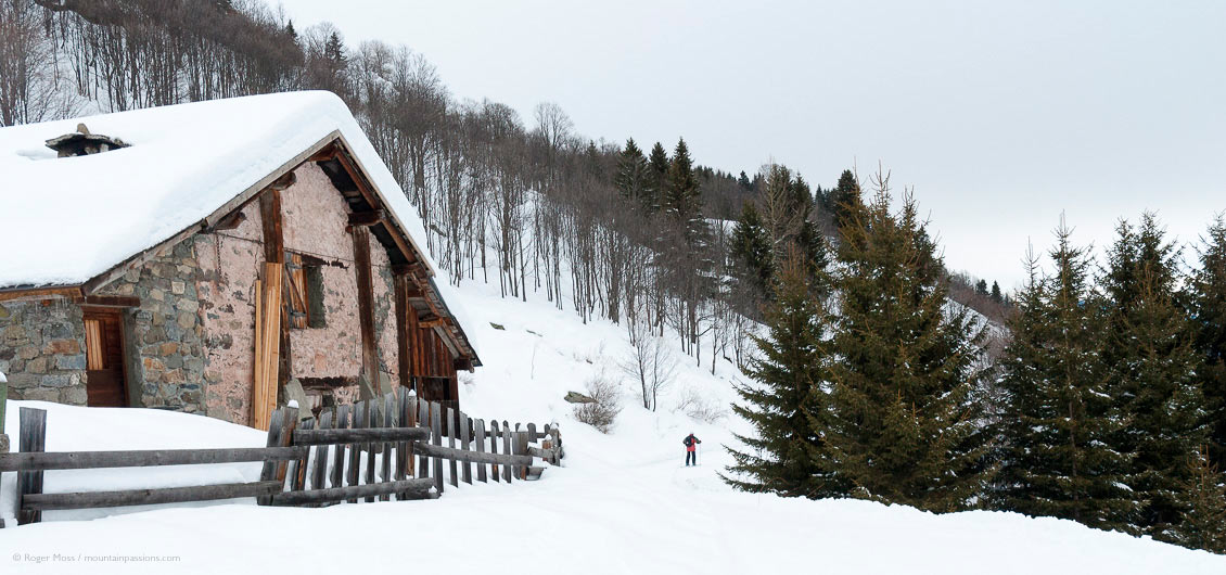 Lone skier on country trail passing mountain chalet, with forests