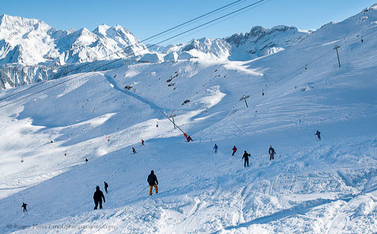 High view of morning skiers descending piste, with chairlift and mountains