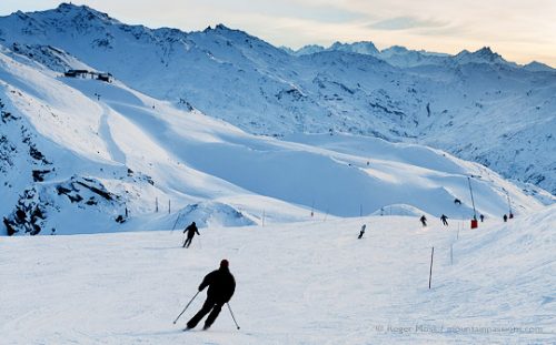 Skiers making final runs in late afternoon, with sun setting