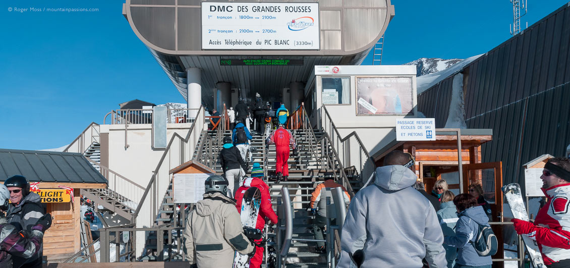 Skiers and snowbaorders climbing steps to gondola ski lift at Alpe d'Huez