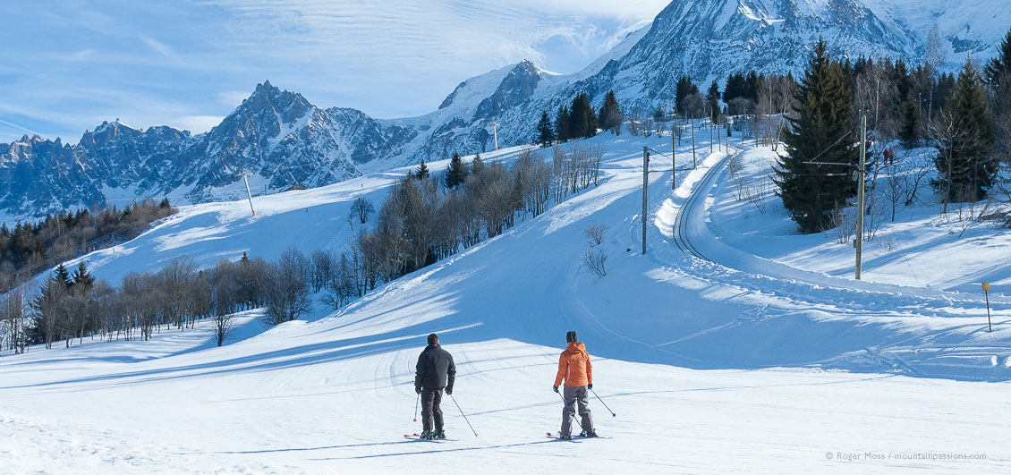 Wide view of two skiers on piste beside Mont Blanc Tramway at Les Houches
