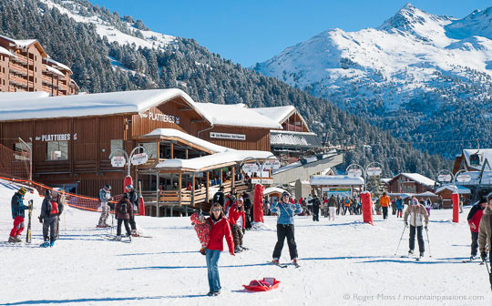 Wide view of skiers moving between lifts, with wooded mountainside in background