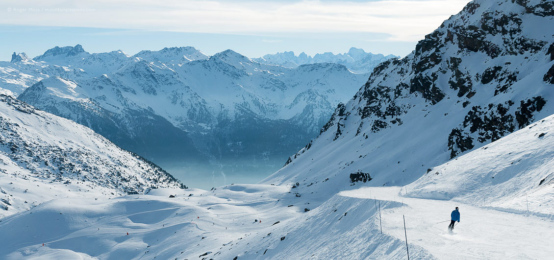 Wide view of of skier on long mountain descent above Orelle