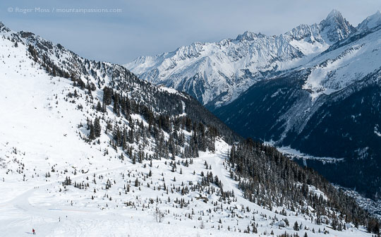 High view of ski pistes on mountainside with valley and mountains