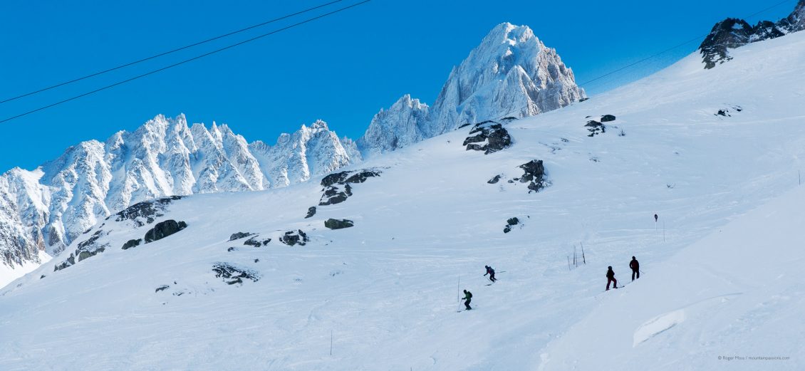 Skiers descending piste above Argentière, with snow-covered peaks in background.