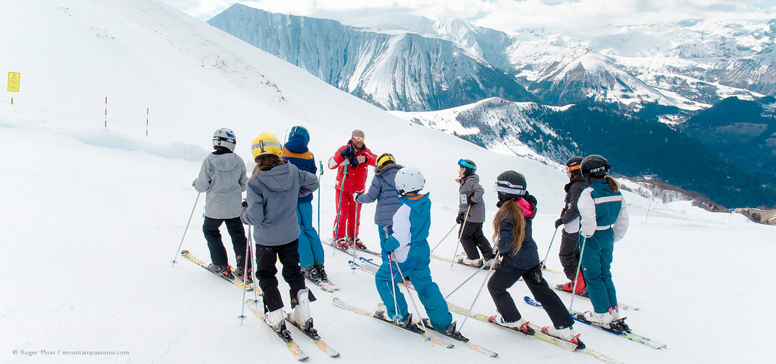 Skie instructor on mountainside with group of young skiers